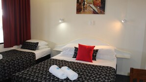Een hotelkamer met twee bedden, elk voorzien van beddengoed met een patroon en kussens, een schilderij aan de muur en een paar handdoeken op het bed.