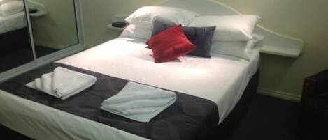 A neatly made bed with white and grey bedding, a red pillow, and a white towel on the bed.