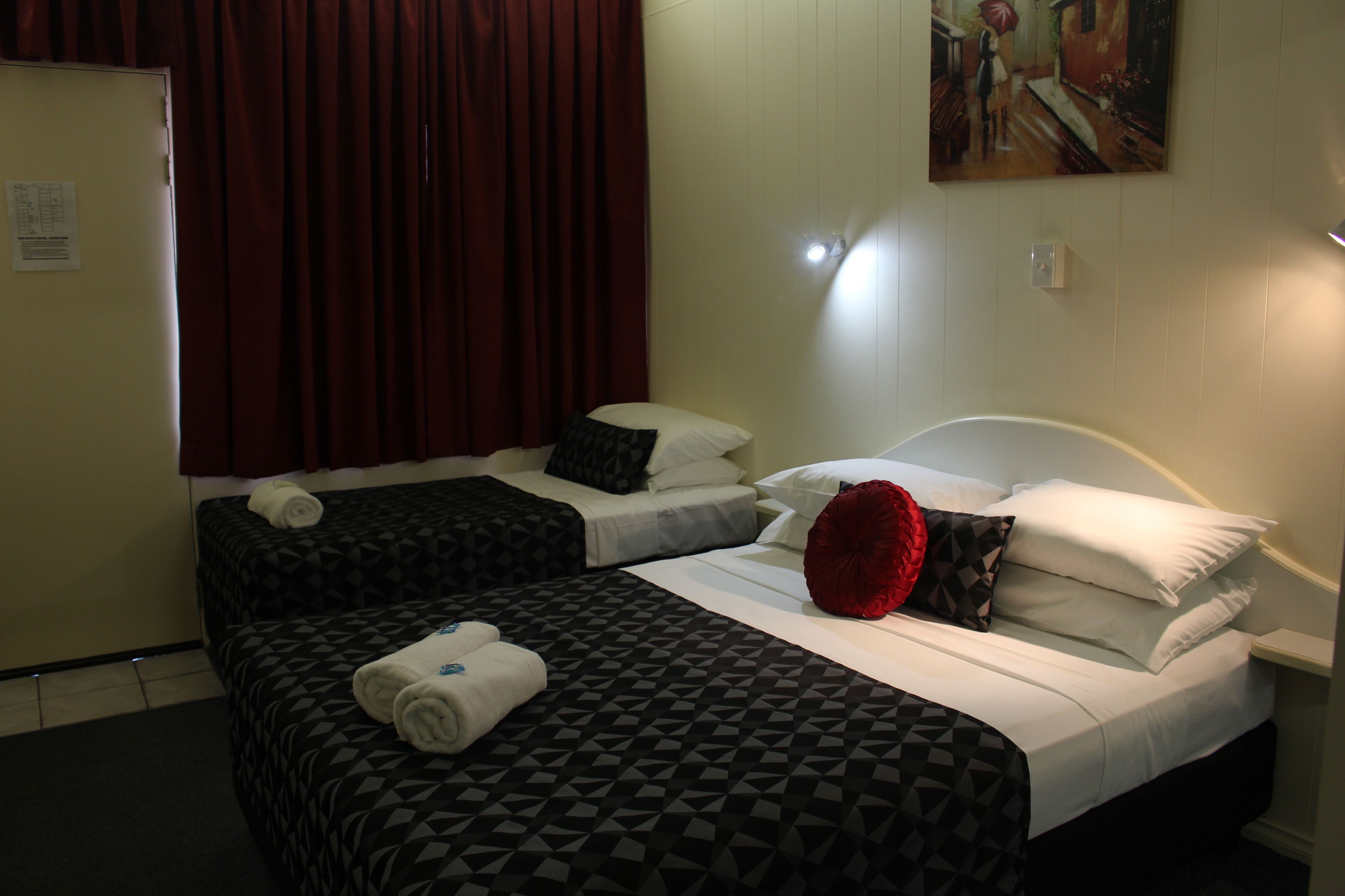 A hotel room with two beds, a red curtain, and a painting on the wall.