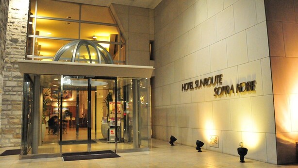 The entrance of Hotel Sunroute Sofra Kobe with a glass facade, a lobby area, and a sign on the wall. - Hotel Sunroute Sopra Kobe (Kobe)