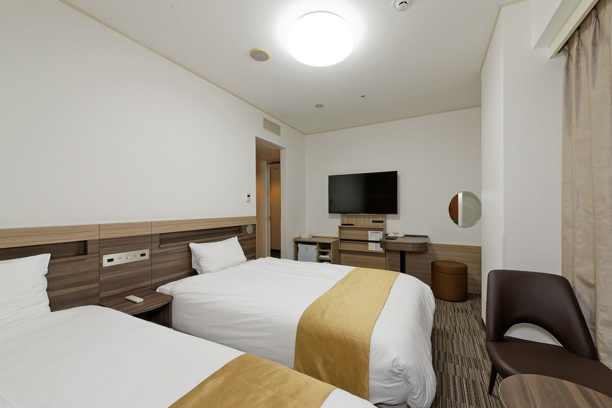 A hotel room with two beds, a television, a desk, and a chair.