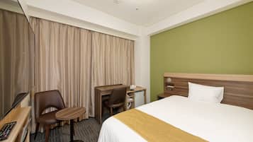 A hotel room with a bed, a desk, a chair, a small table, and a television.