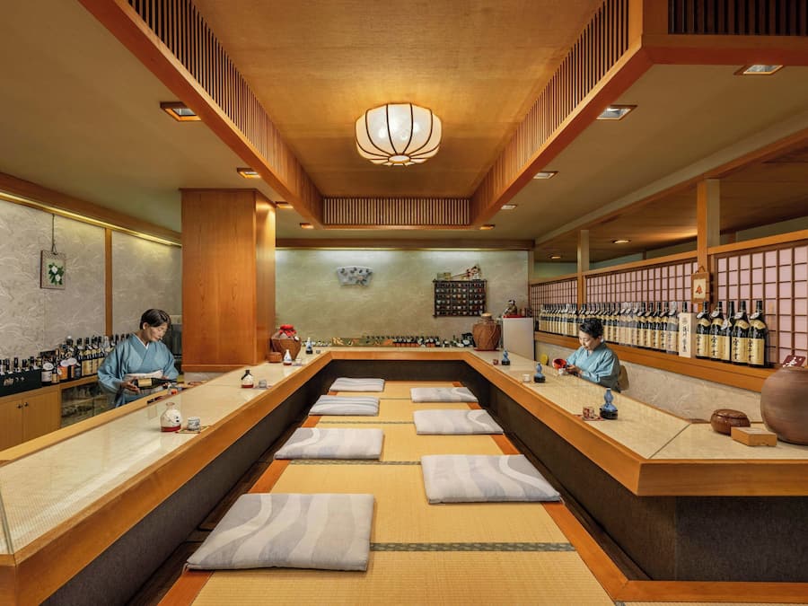 Una casa de té japonesa tradicional con esteras de tatami, mobiliario de madera y una exhibición de botellas de sake.