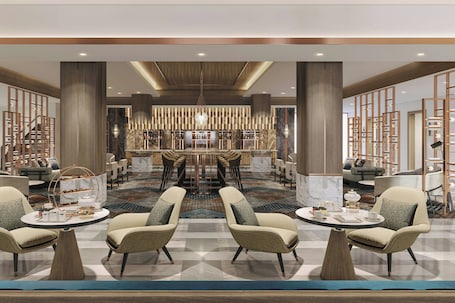 A spacious lobby with a central seating area, a bar, and a staircase.