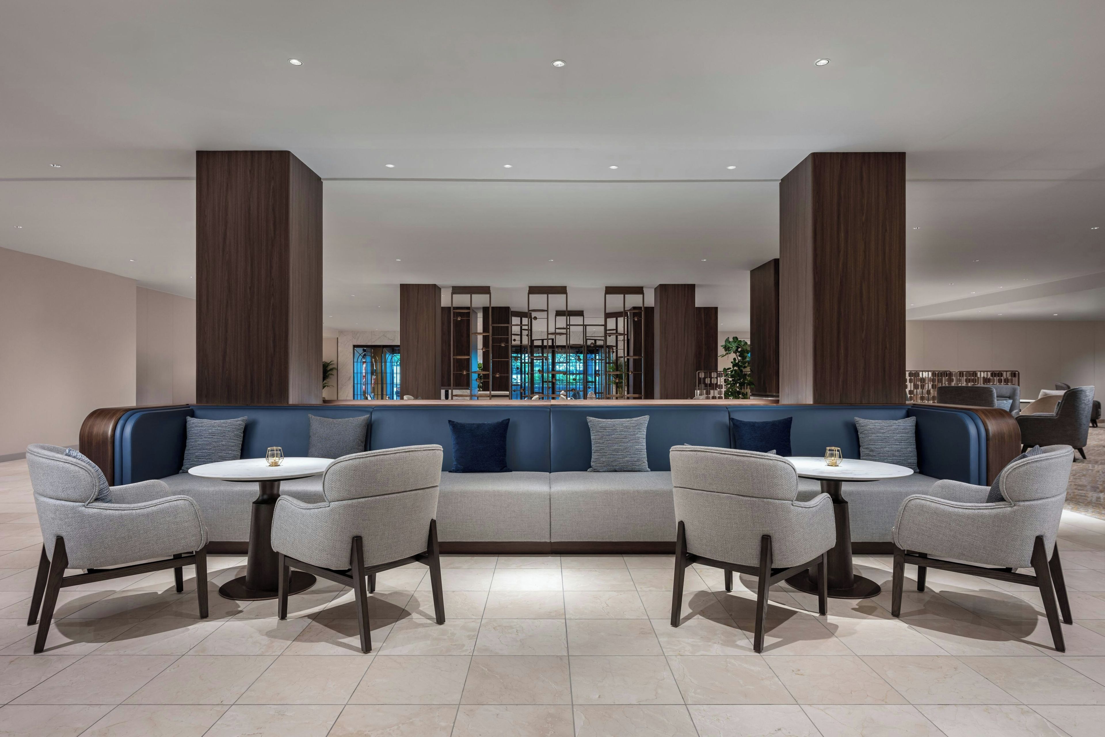 A modern lounge area with a blue sofa, grey armchairs, and a round table.