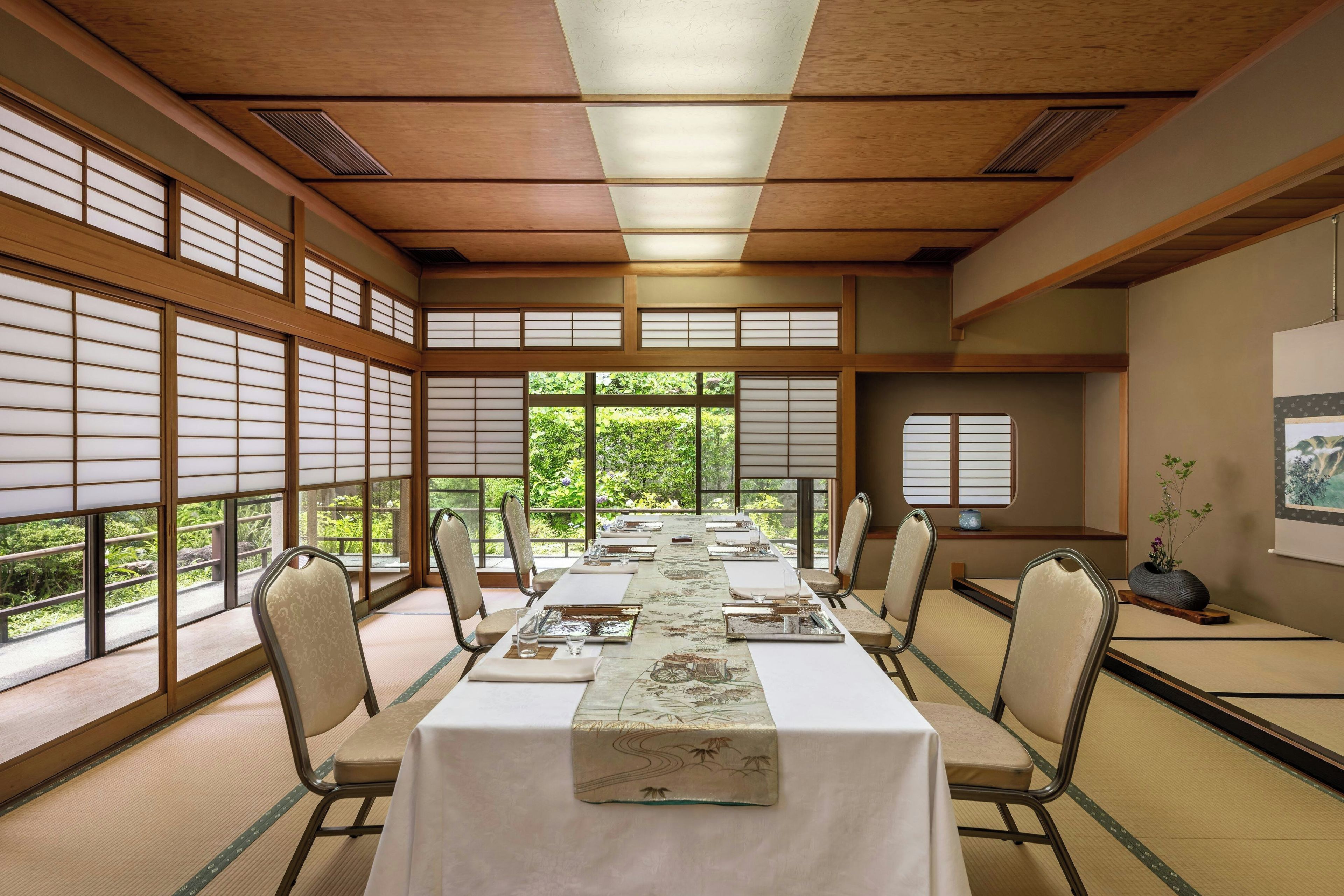 A conference room with tatami mat flooring, a long table set for a meeting, and large windows with a view of greenery.