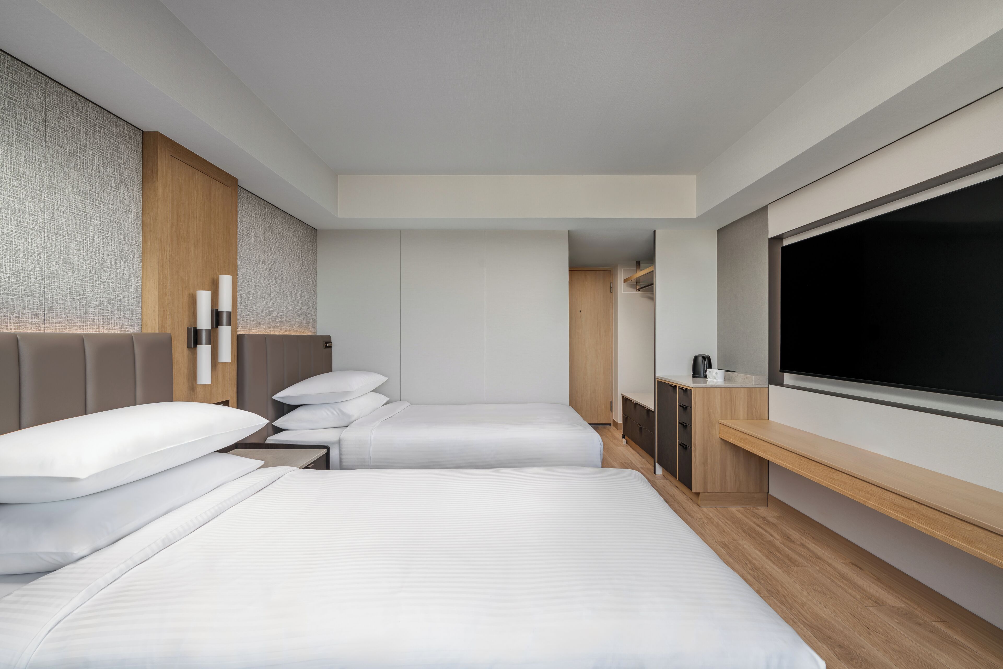 Une chambre d’hôtel moderne équipée d’un grand lit, d’un lit plus petit, d’un bureau et d’une télévision.