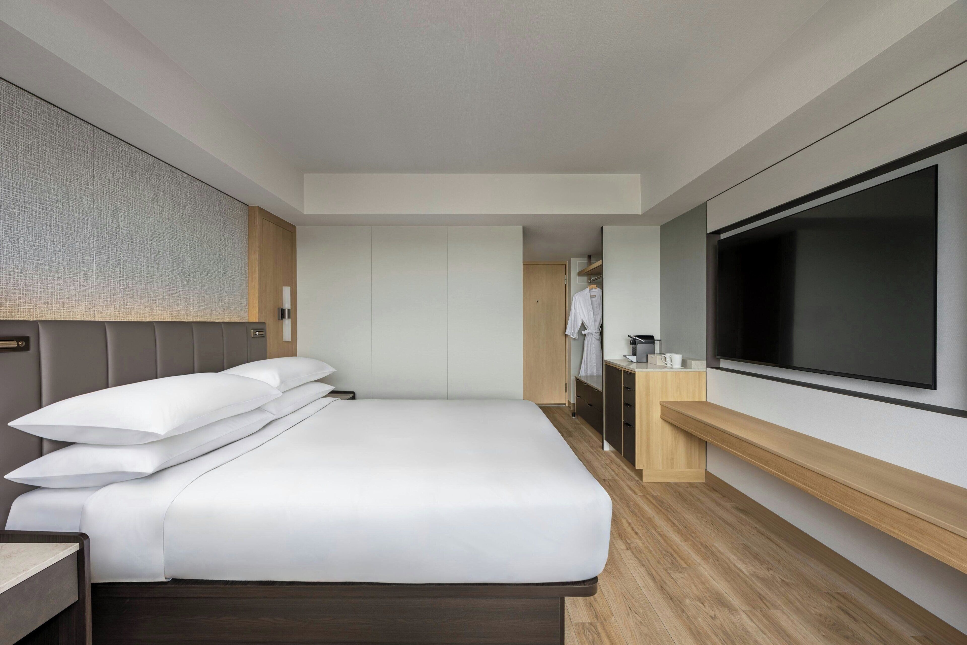 A modern hotel room with a large bed, a flat-screen TV, and a wooden desk.