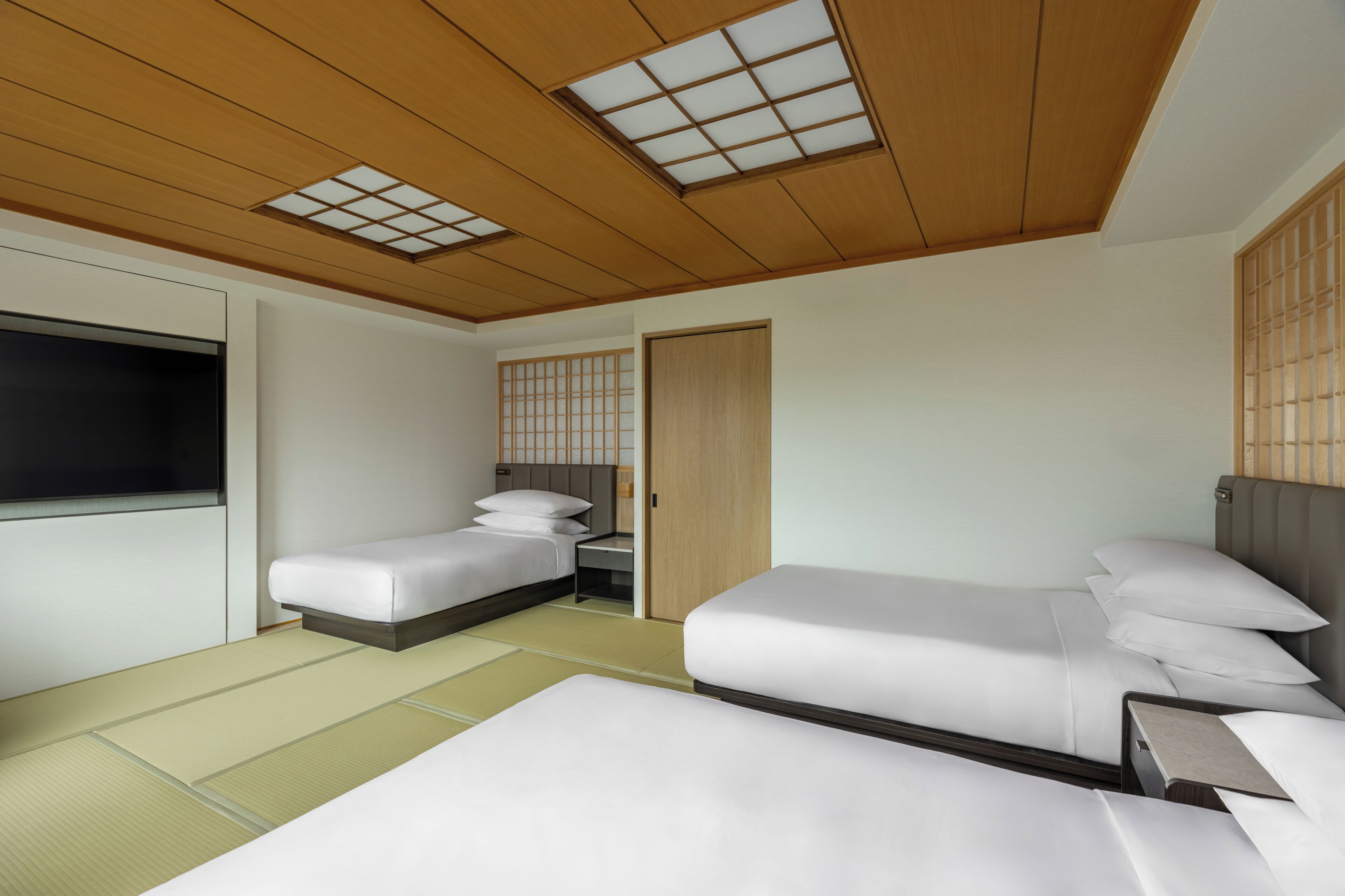 Ein Hotelzimmer mit zwei Betten, einem Fernseher und einer Schiebetür.