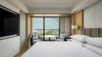 A hotel room with a large bed, a TV, a balcony with a table and chairs, and a city view.