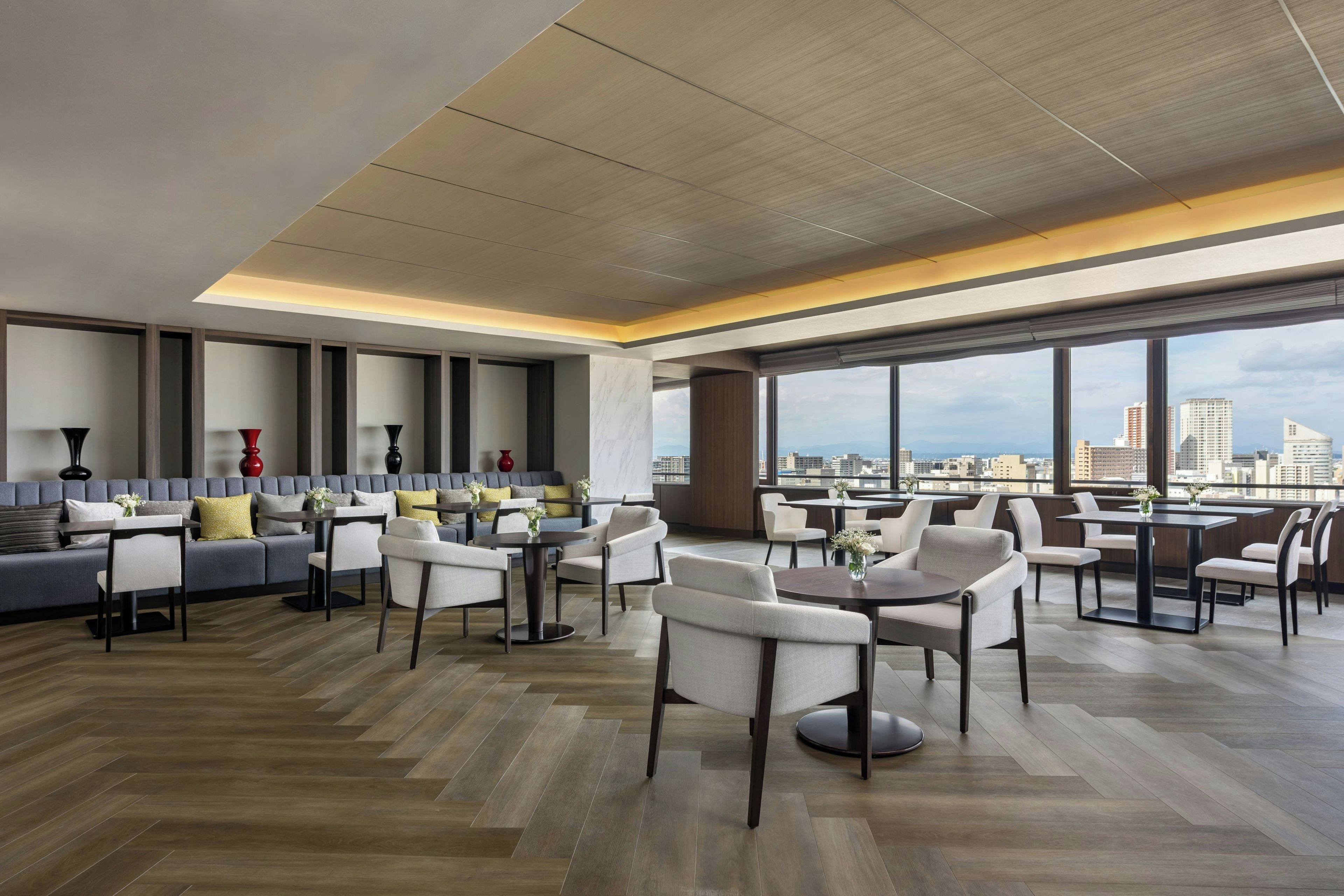 Un hall d’hôtel moderne avec vue sur la ville, comprenant différents espaces de détente et des tables.