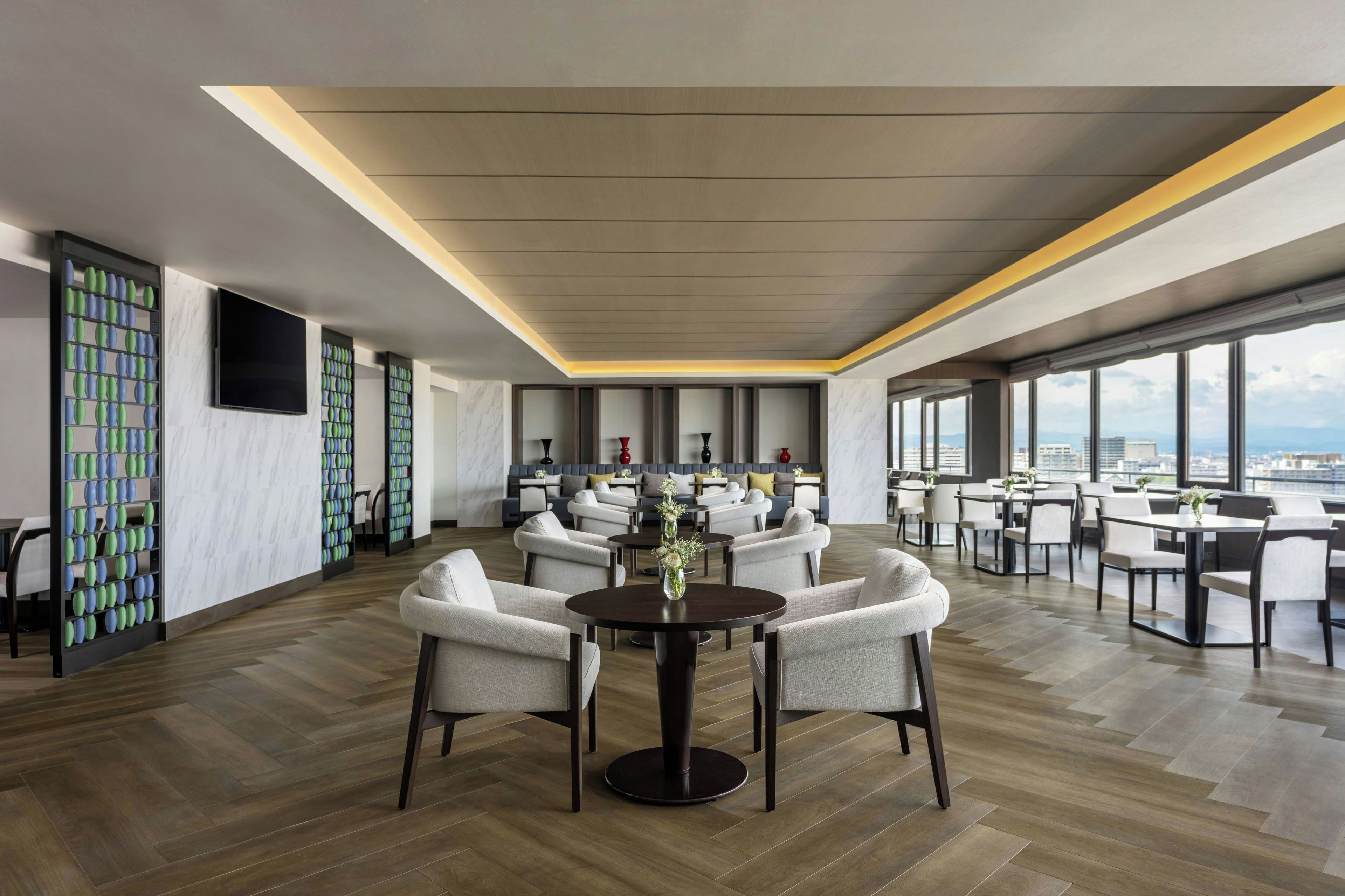 A modern hotel lobby with a high ceiling, marble flooring, and a seating area with round tables and chairs.