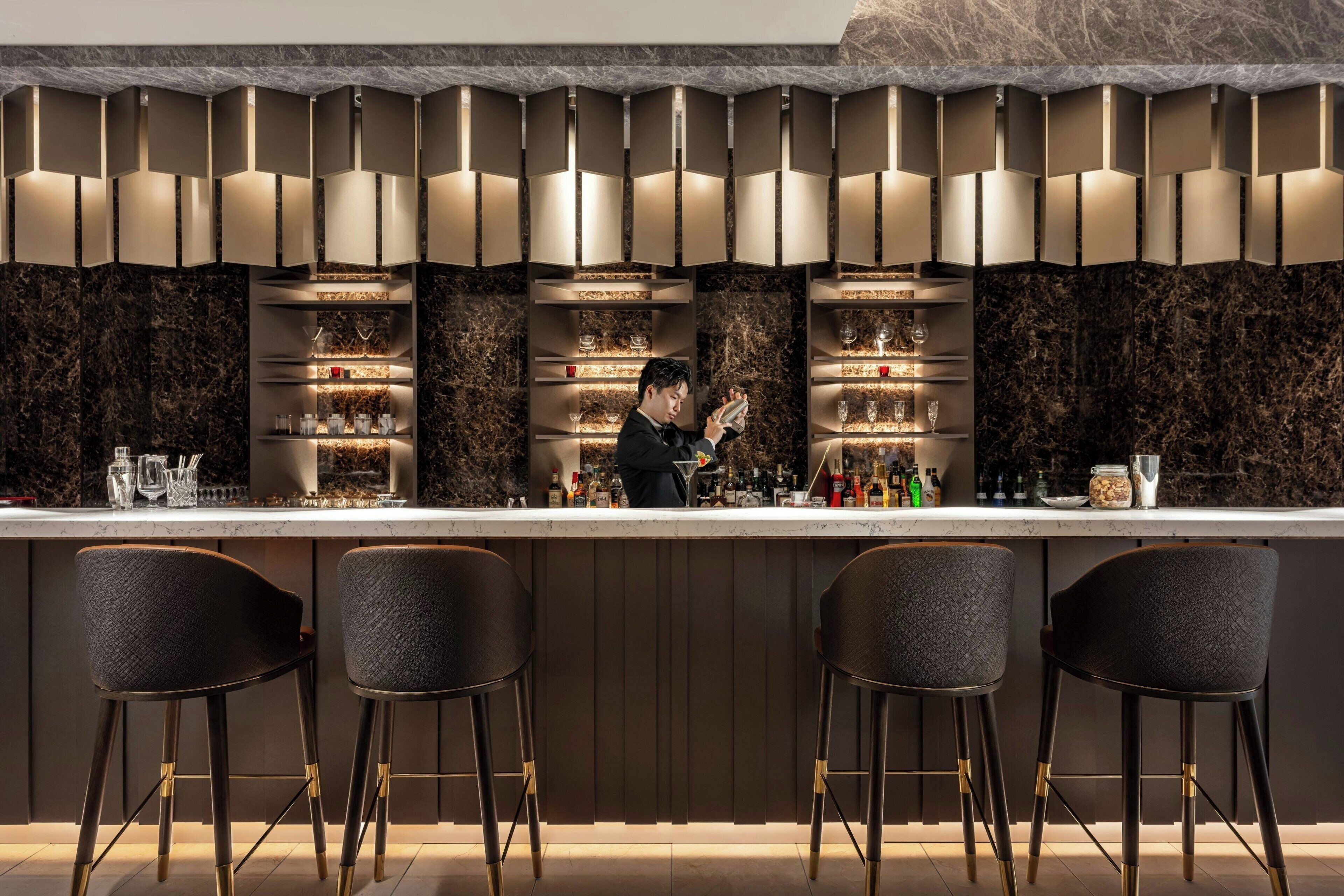 A bar area with a marble countertop, shelves with glasses, and stools.