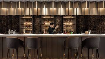 A bar area with a marble countertop, shelves with glasses, and stools.