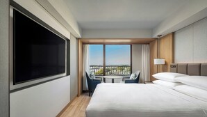 Habitación de hotel con una cama grande, televisión, balcón con mesa y sillas, y vista a la ciudad.