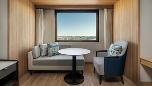 Una habitación moderna con sofá, una silla, una mesa redonda y un ventanal con vista a la ciudad.
