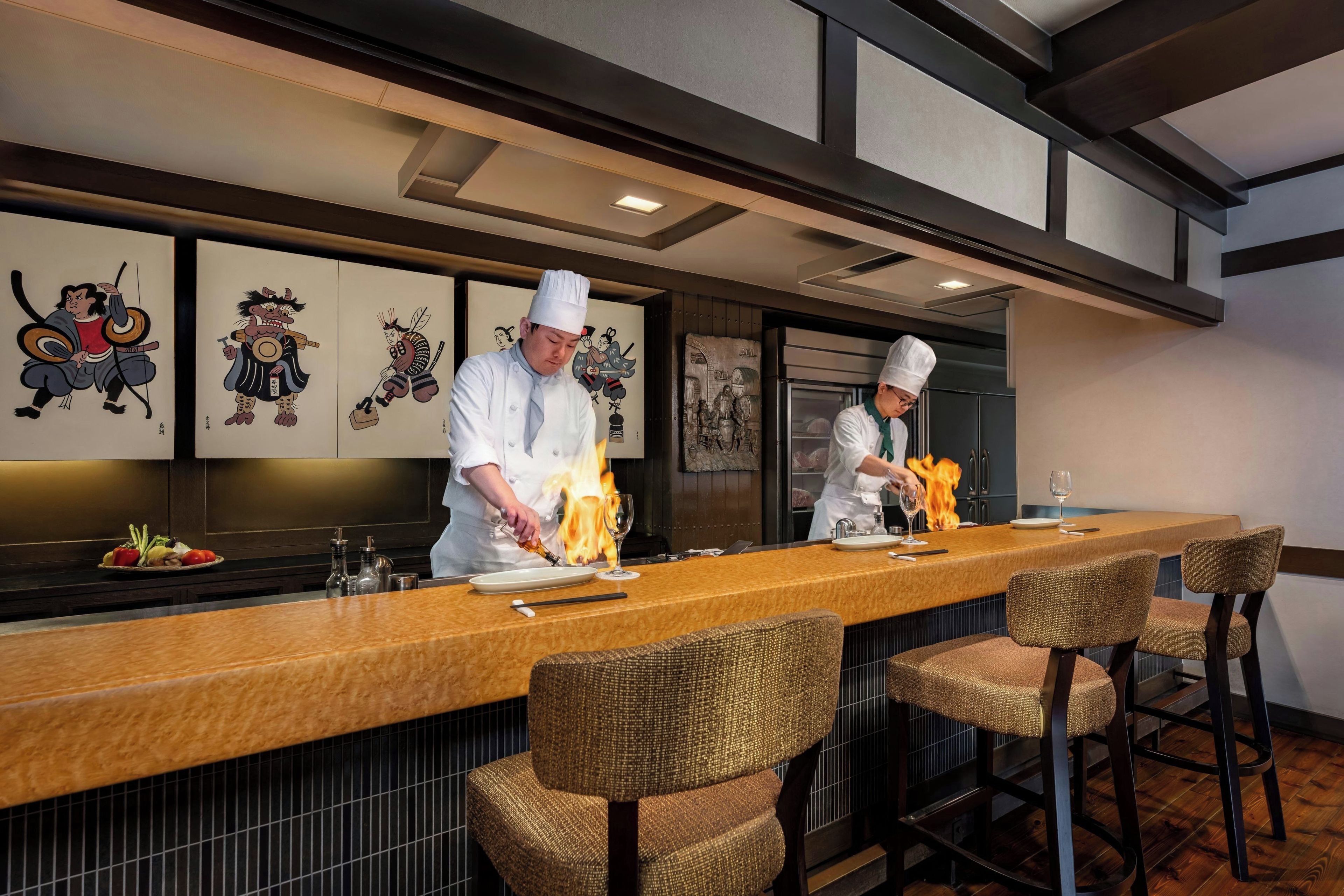 A restaurant with a long counter, bar stools, and a wall with traditional artwork.