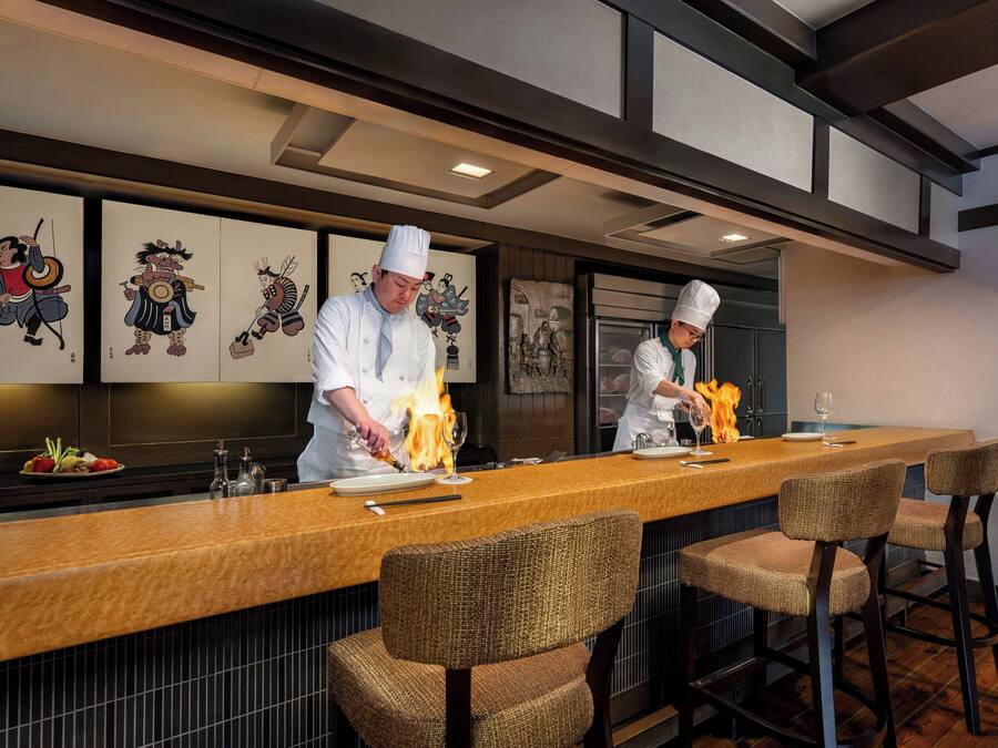 A restaurant with a long counter, bar stools, and a wall with traditional artwork.