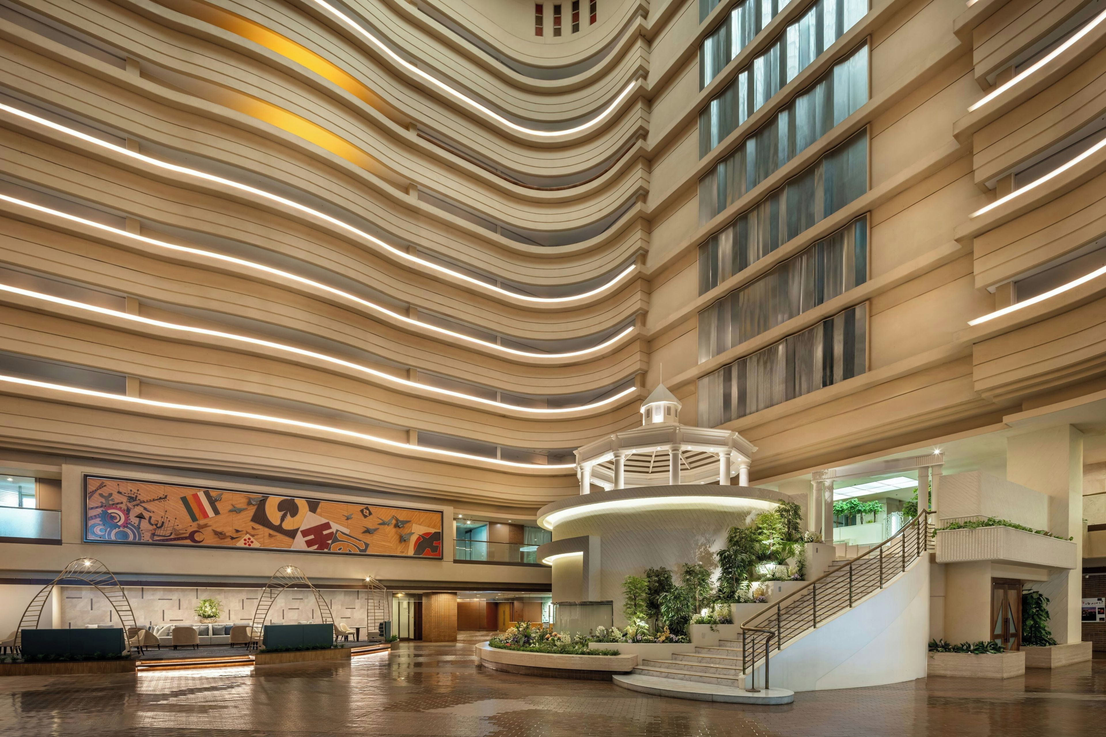 A spacious lobby with a central staircase, a large mural, and a modern ceiling design.