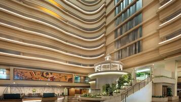 A spacious lobby with a central staircase, a large mural, and a modern ceiling design.