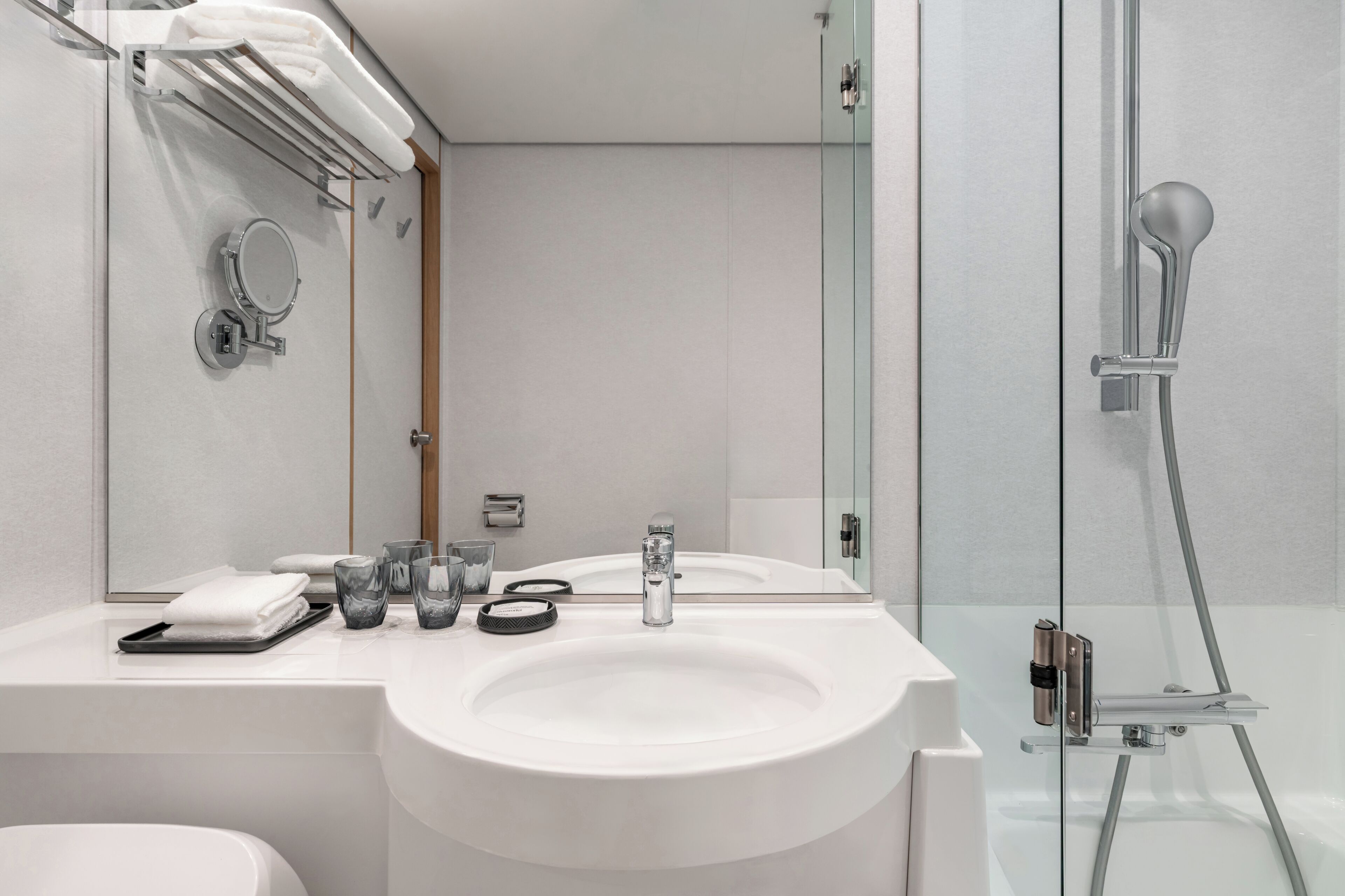 A modern bathroom with a white sink, mirror, and glass shower enclosure.