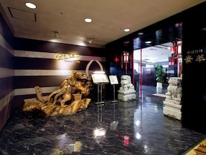 Un hall d’entrée orné d’une sculpture en bois, une enseigne indiquant « Go-ka, restaurant chinois », et un comptoir d’accueil.