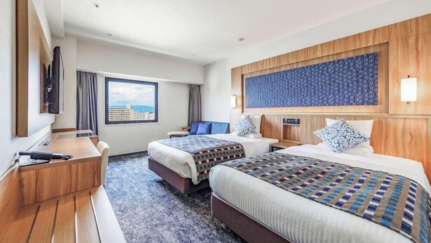 A hotel room with two beds, a desk, a TV, and a large window with a view.