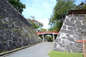 A stone bridge over a road with a red railing, surrounded by greenery and a clear sky.