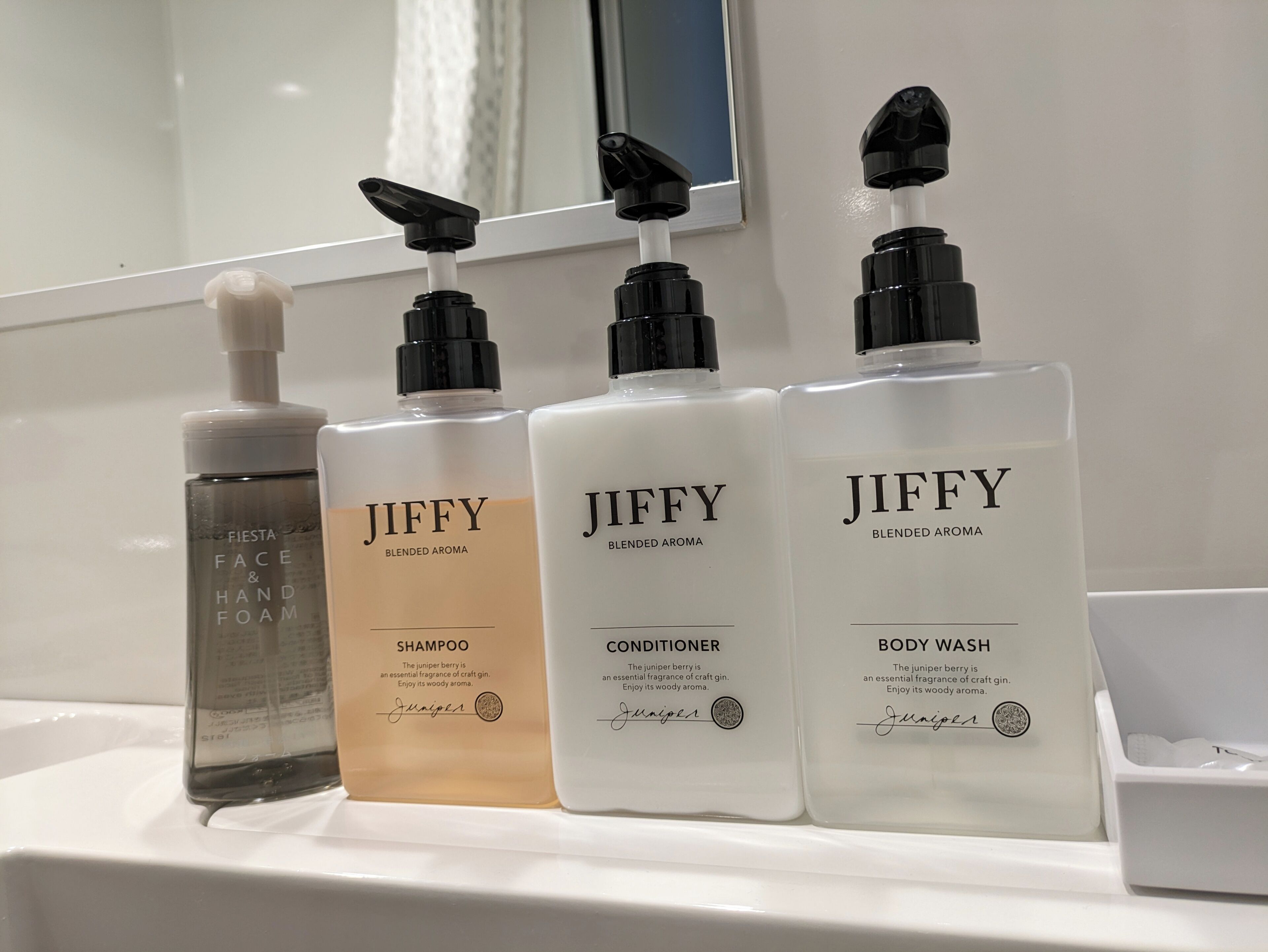 A bathroom shelf with four Jiffy brand toiletries: a face and hand foam, a shampoo, a conditioner, and a body wash.