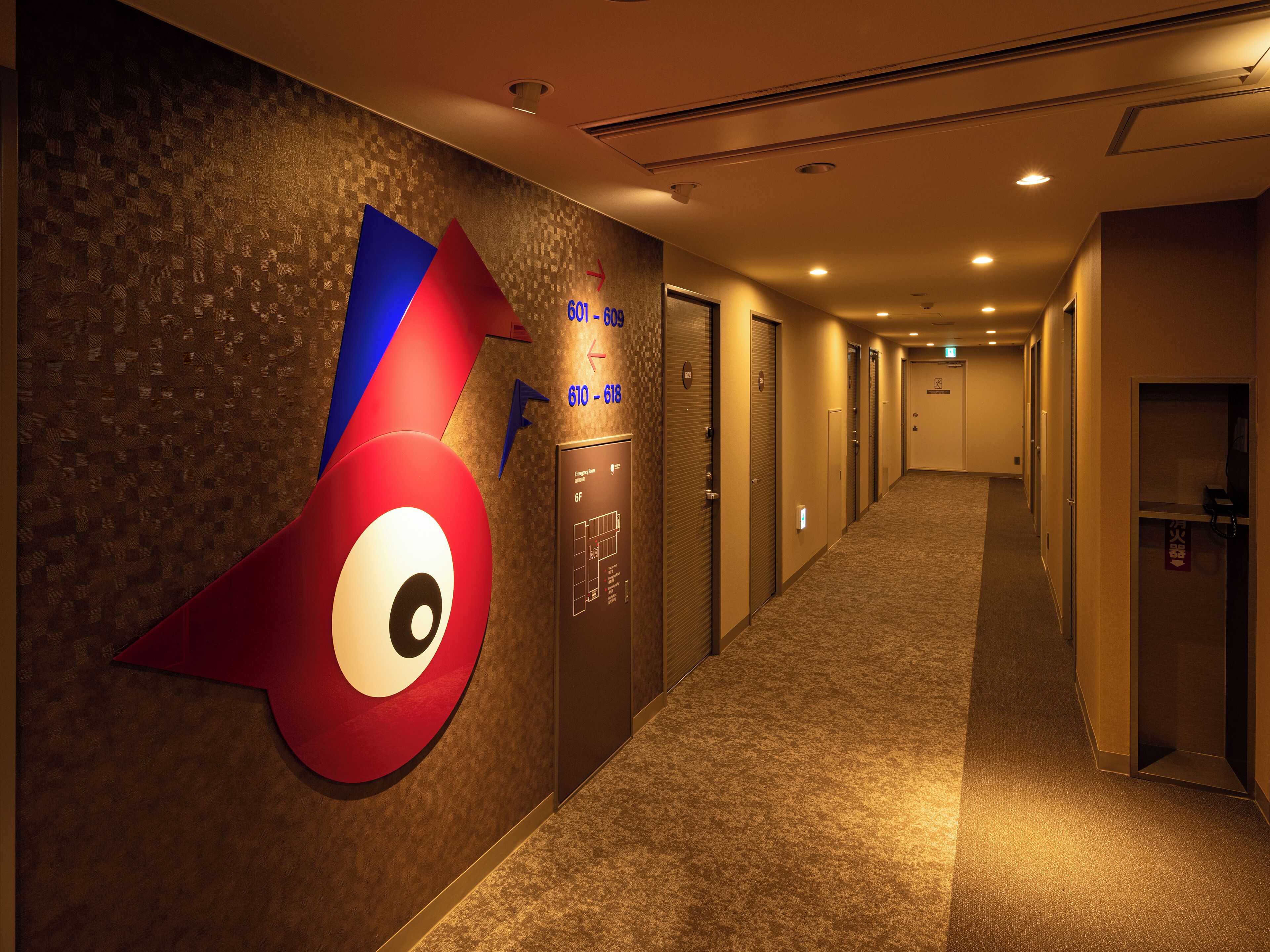 A hotel corridor with a large wall art piece, multiple doors, and a carpeted floor.