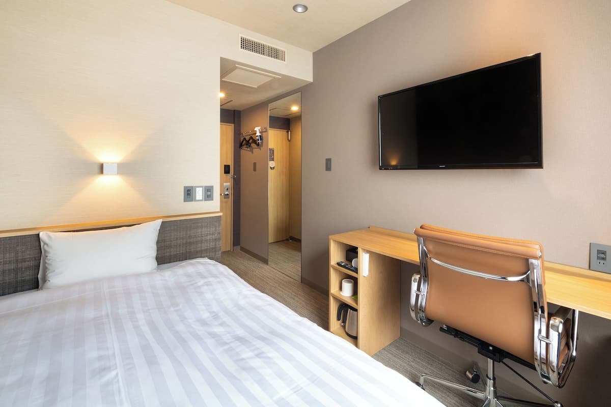 A hotel room with a bed, a desk, a chair, a television, and a bathroom visible through an open door.