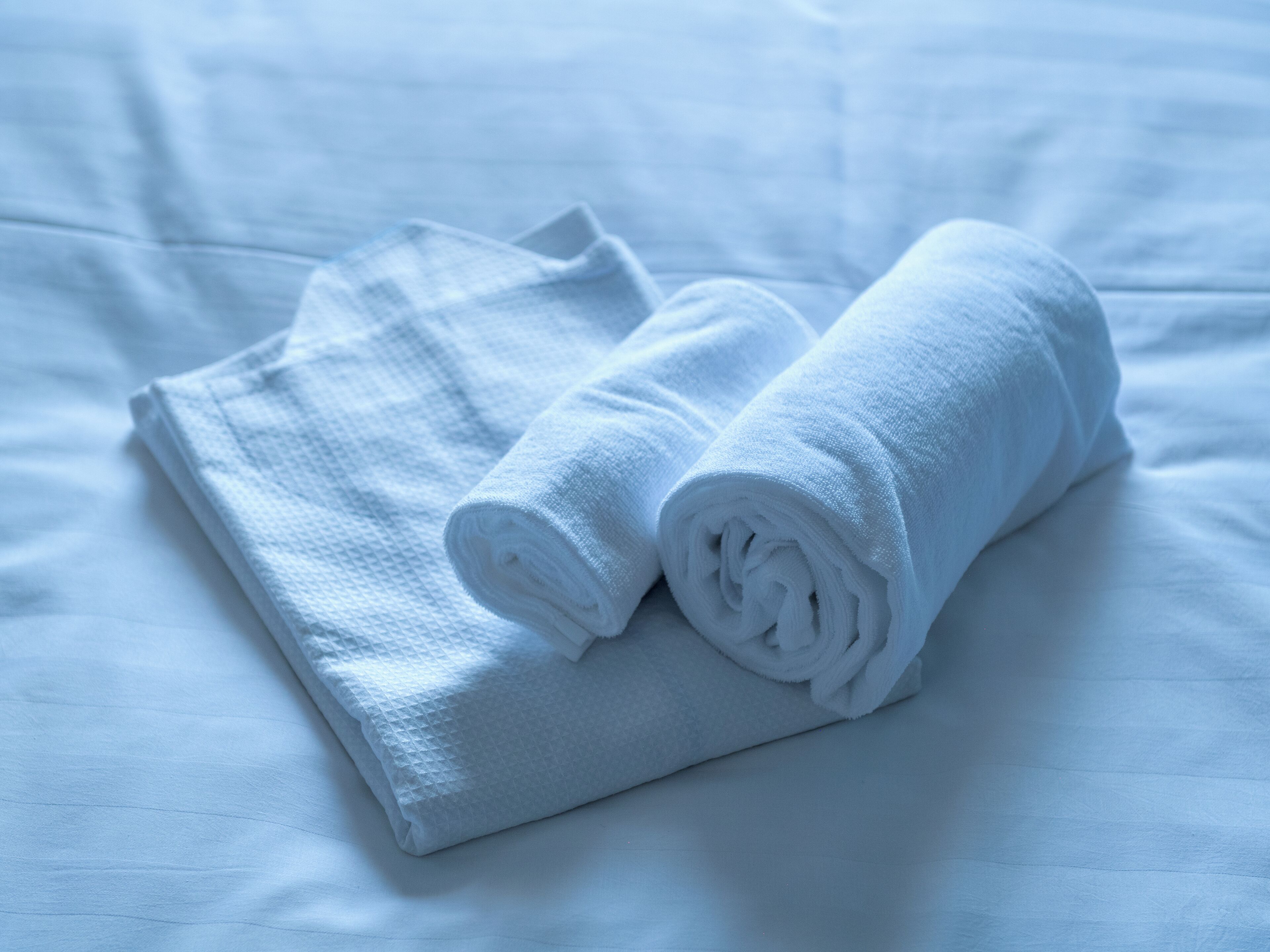 A neatly folded white towel on a bed with a smooth, white sheet.