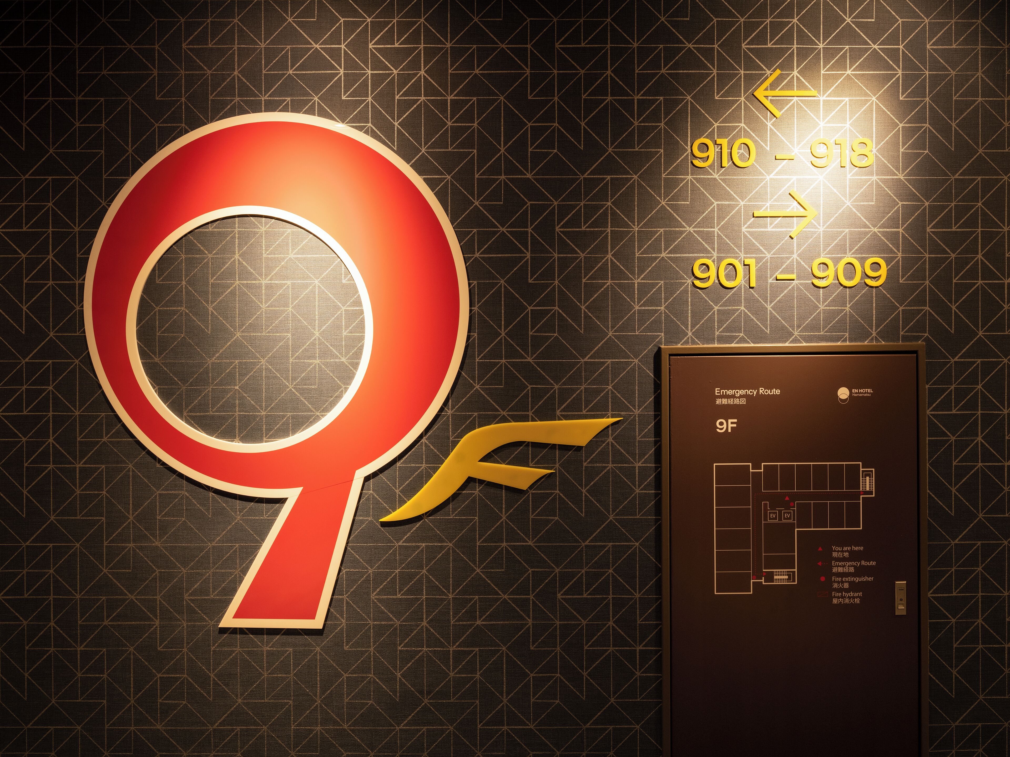 A large red and gold emergency route sign with directional arrows and room numbers 910-918 and 901-909.