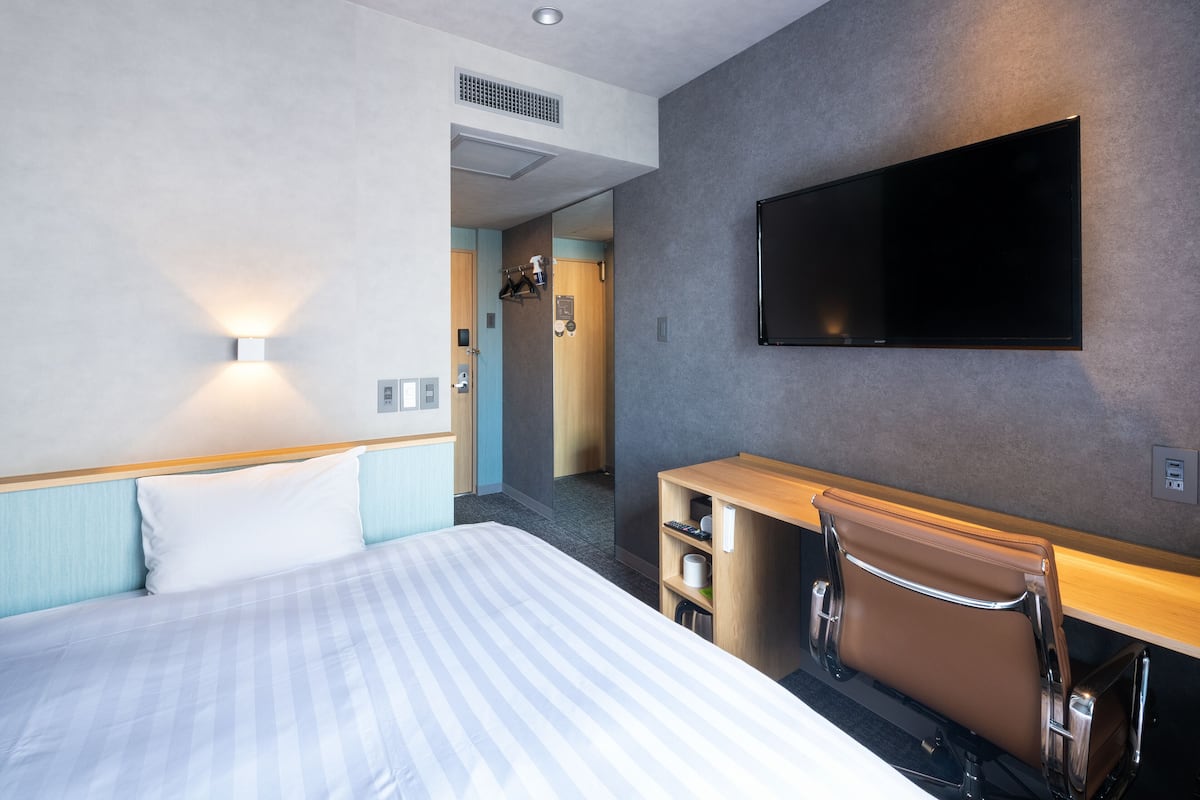 A hotel room with a bed, a desk, a chair, a television, and a bathroom door.