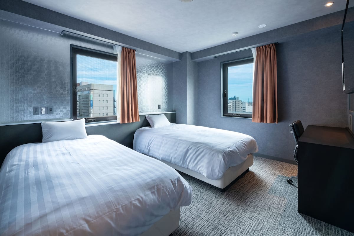 A modern hotel room with two beds, large windows, and a view of the city.