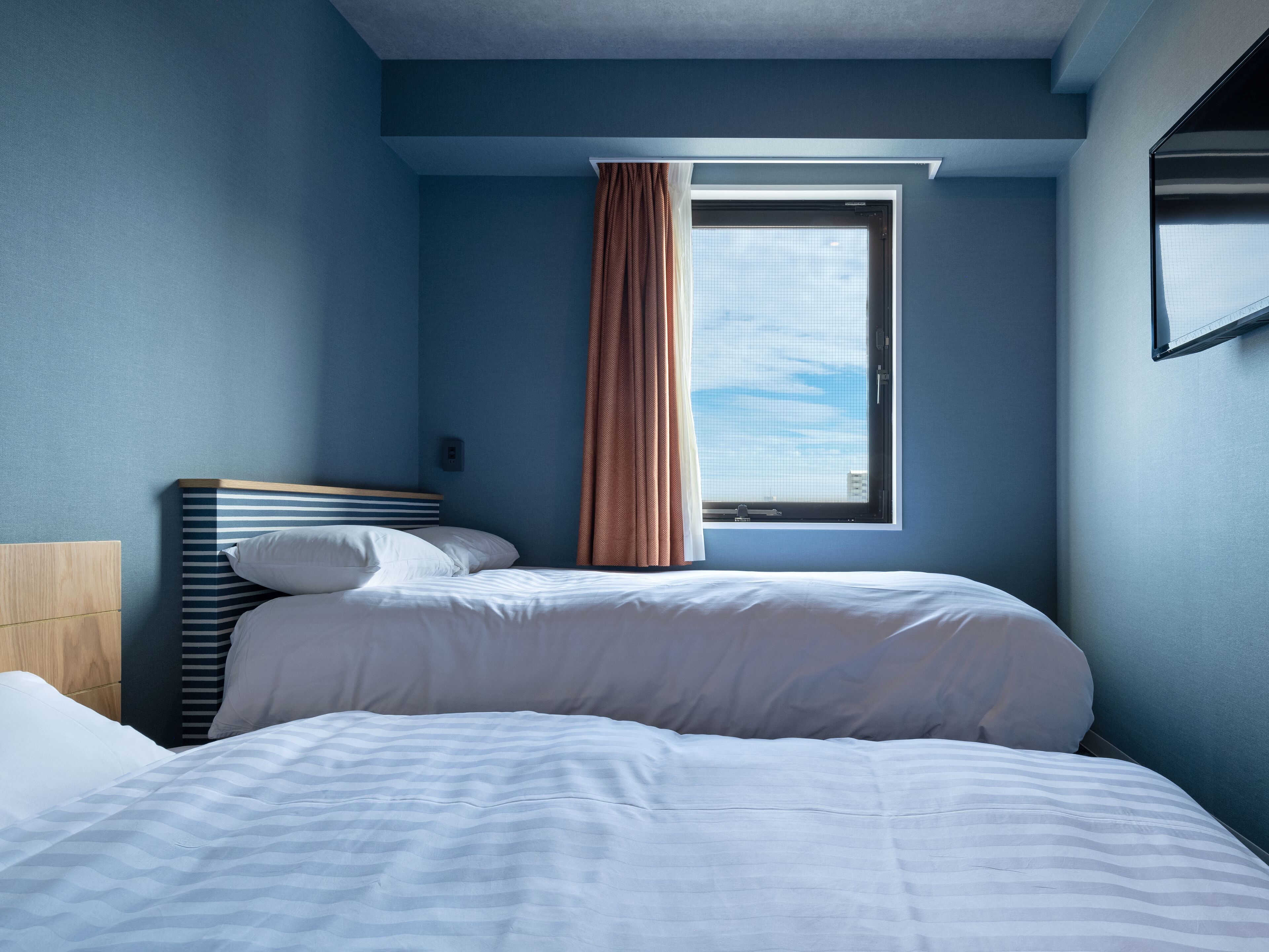 A hotel room with a bed, a window with curtains, and a view of the sky.