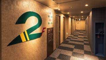 Un couloir d’hôtel avec un tapis à carreaux, des portes numérotées et une grande enseigne « 2F » sur le mur.
