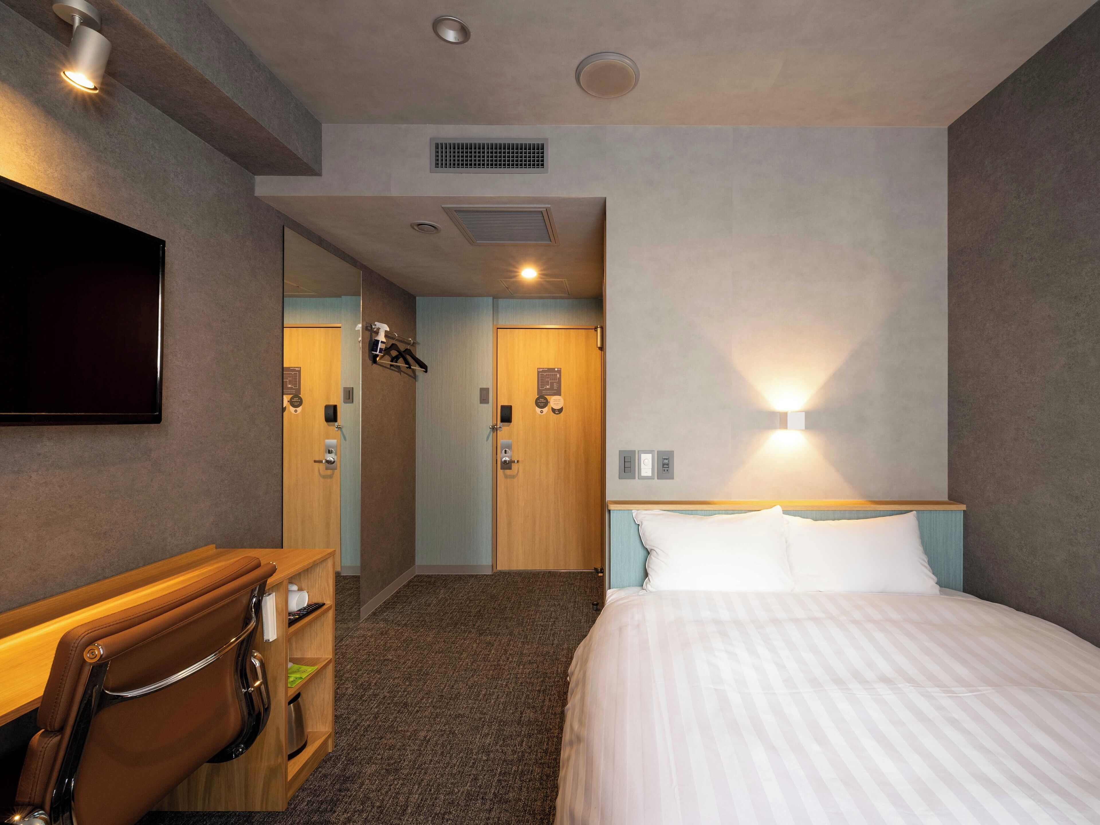 Una habitación de hotel con cama, escritorio, silla, televisión y baño con ducha e inodoro.