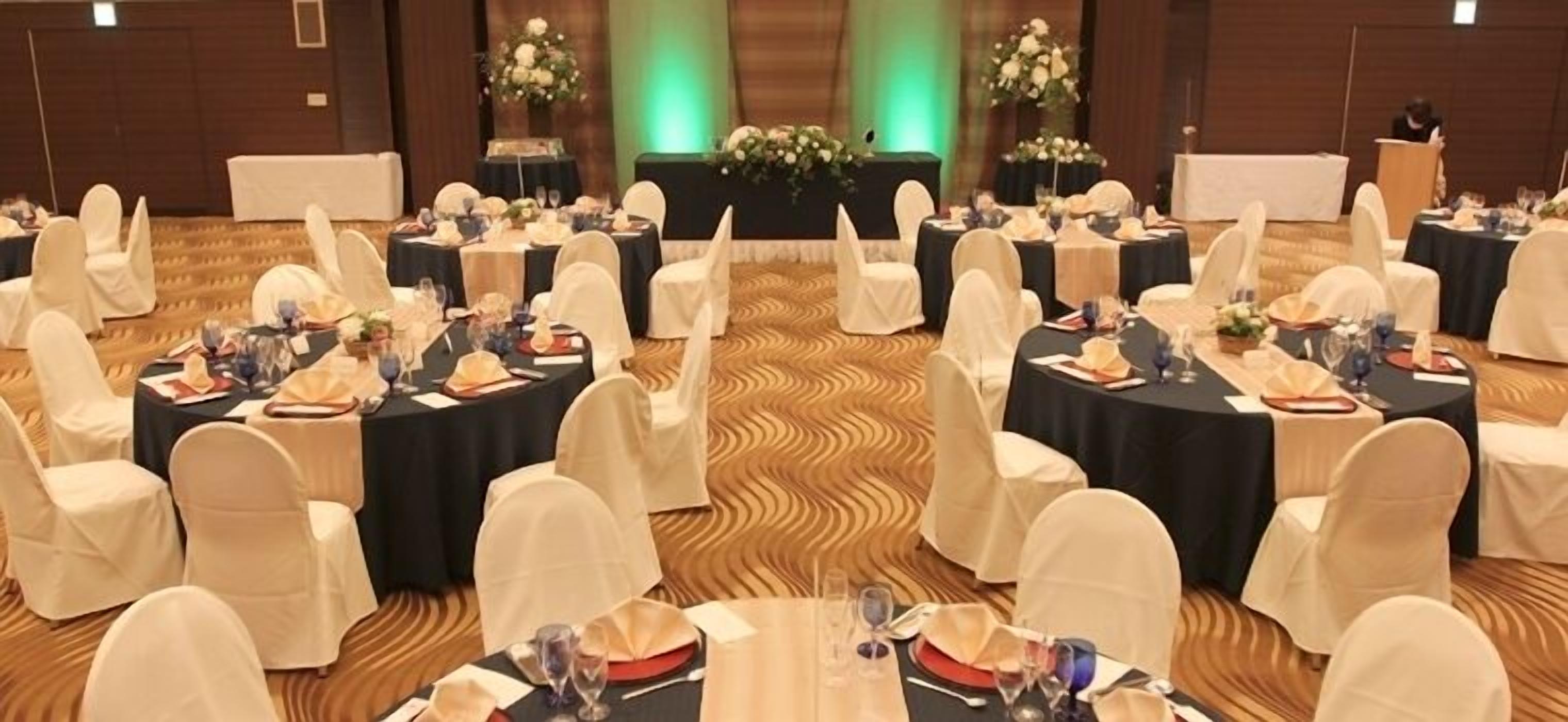 A banquet hall with round tables set for a formal event, featuring white chairs and black tablecloths.