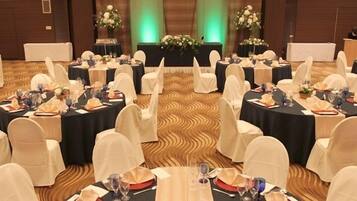 A banquet hall with round tables set for a formal event, featuring white chairs and black tablecloths.