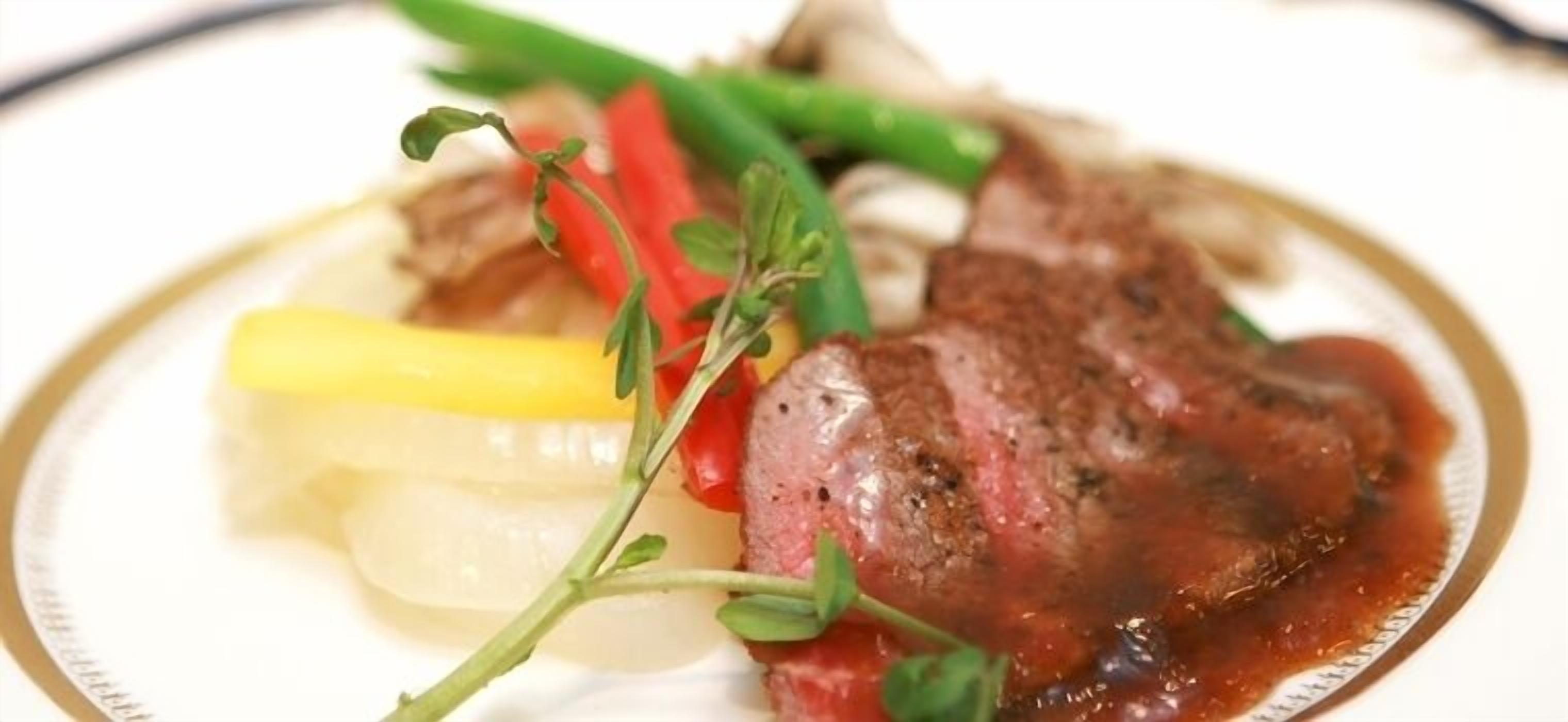 A plate of food with a steak, vegetables, and a garnish.