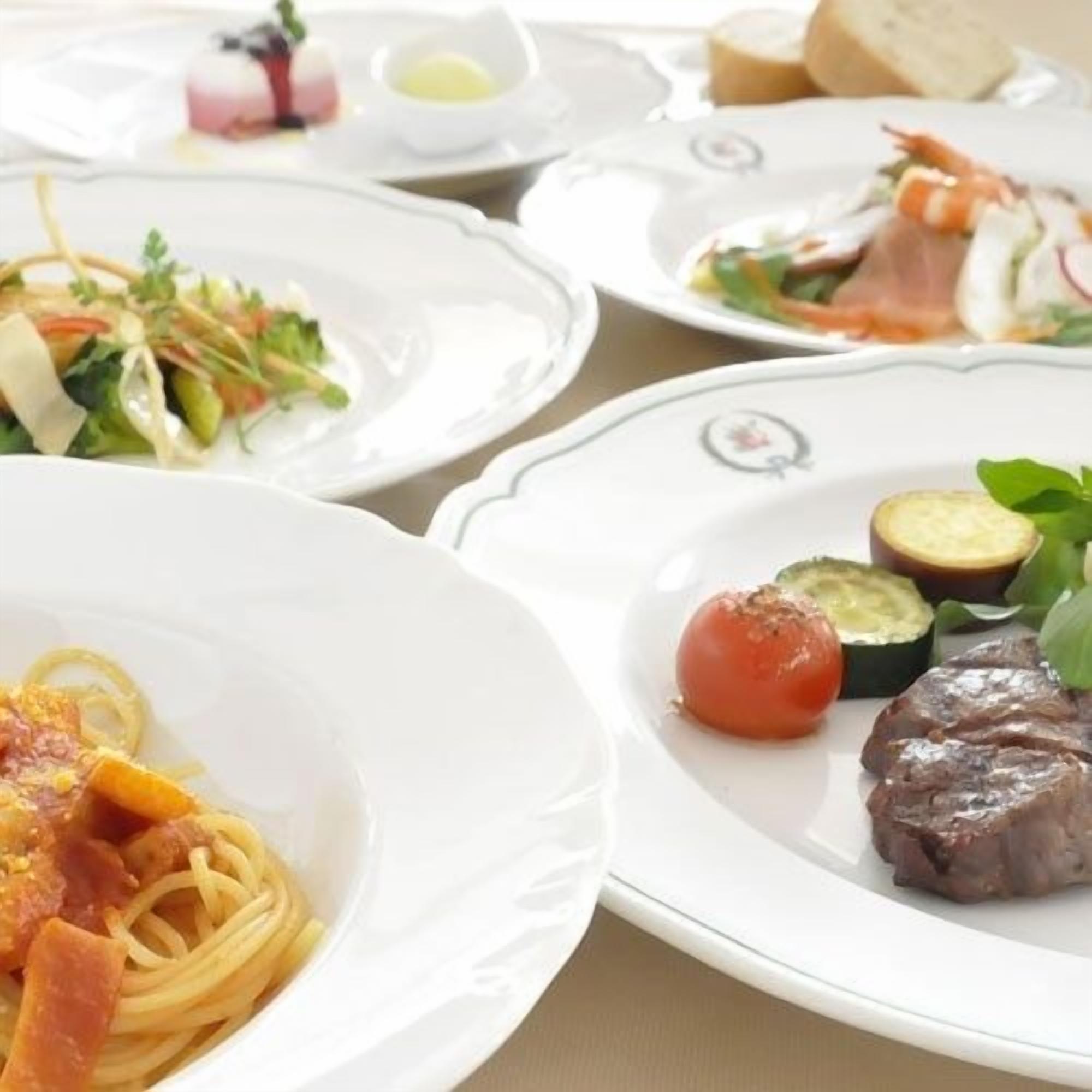 A dining table with various plates of food, including pasta, vegetables, and meat.