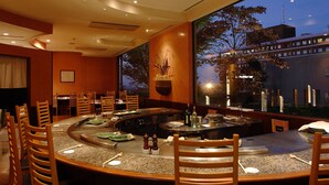 A restaurant with a round table, wooden chairs, and a view of a building outside.