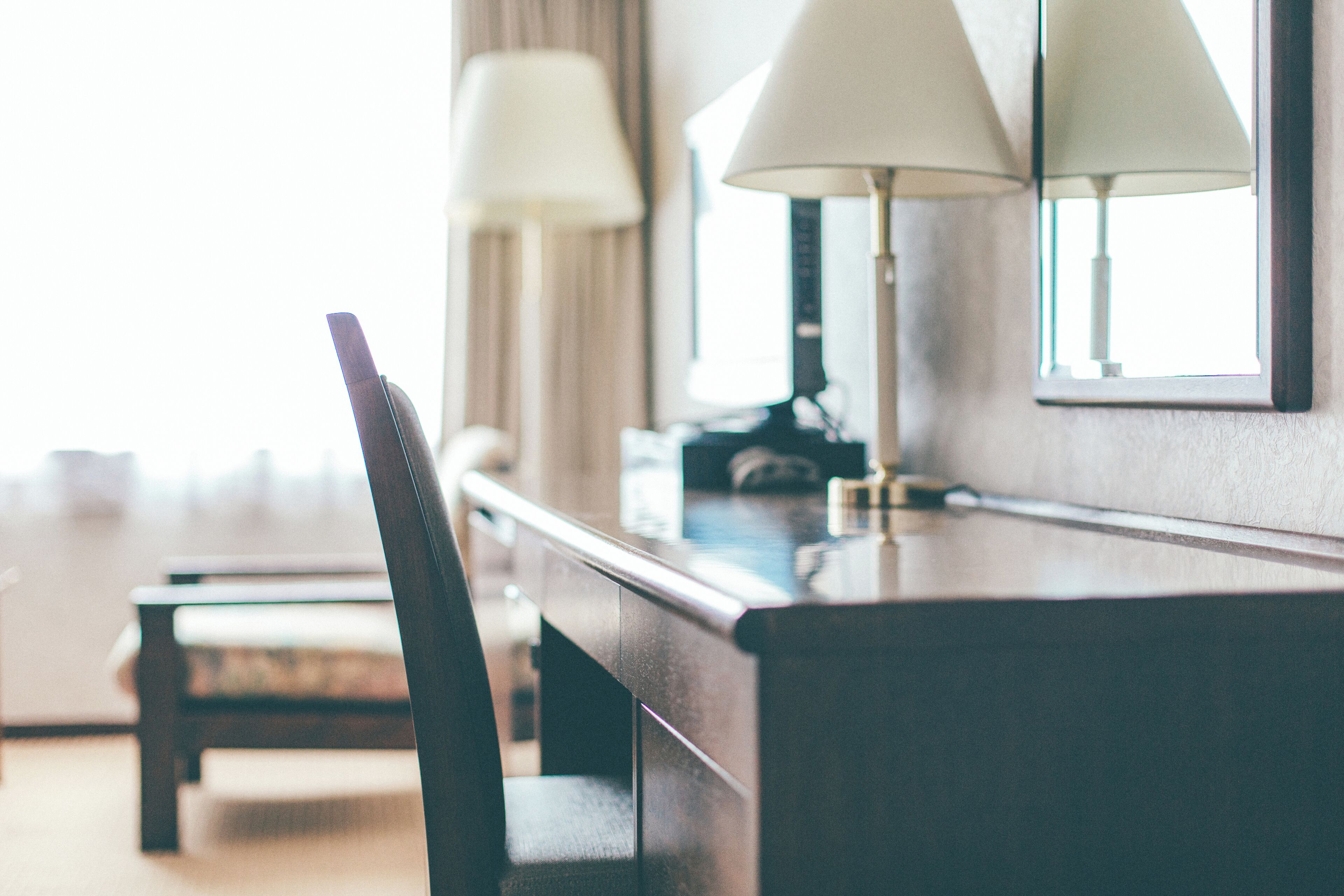 A hotel room with a wooden desk, two lamps, and a mirror.