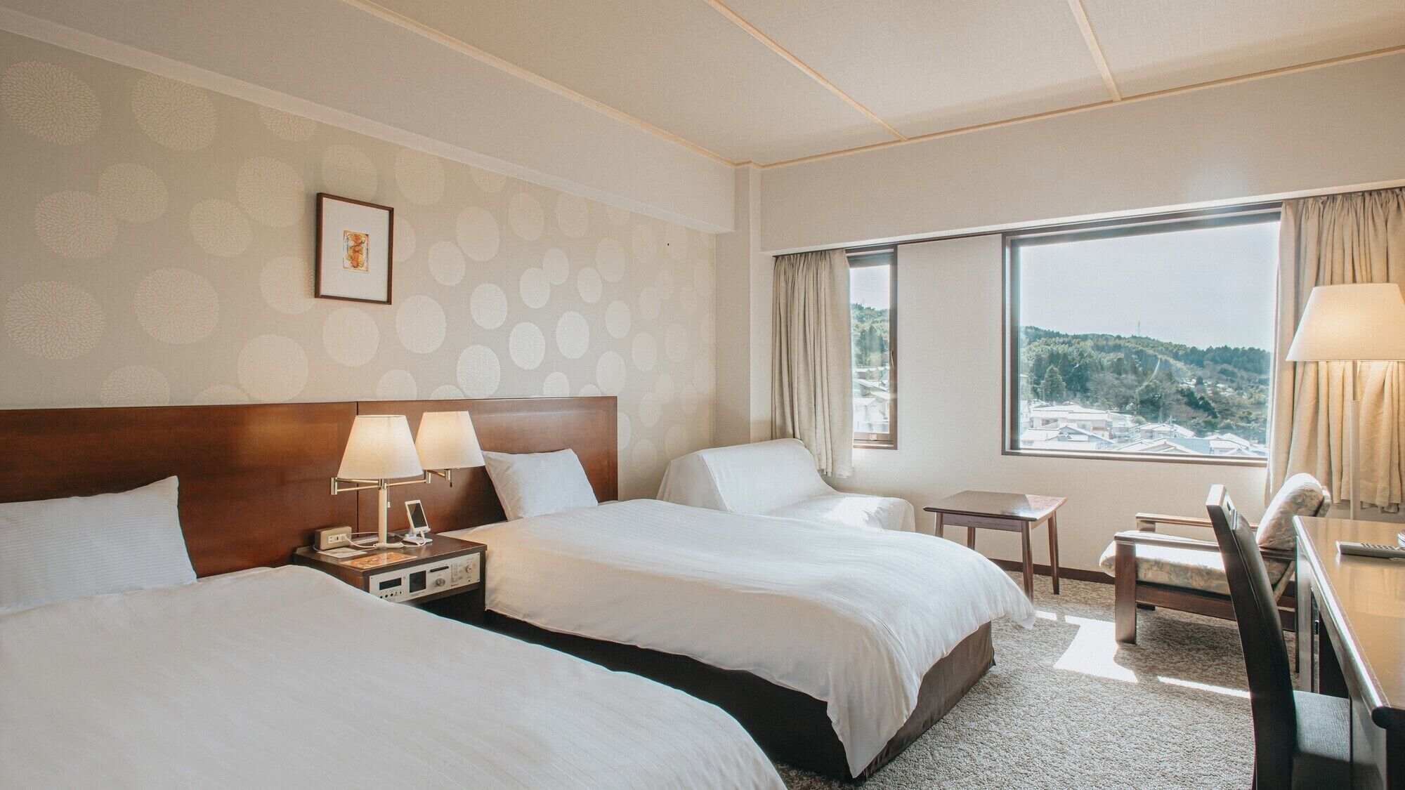 A hotel room with two beds, a desk, a chair, a window with a view, and a framed picture on the wall.