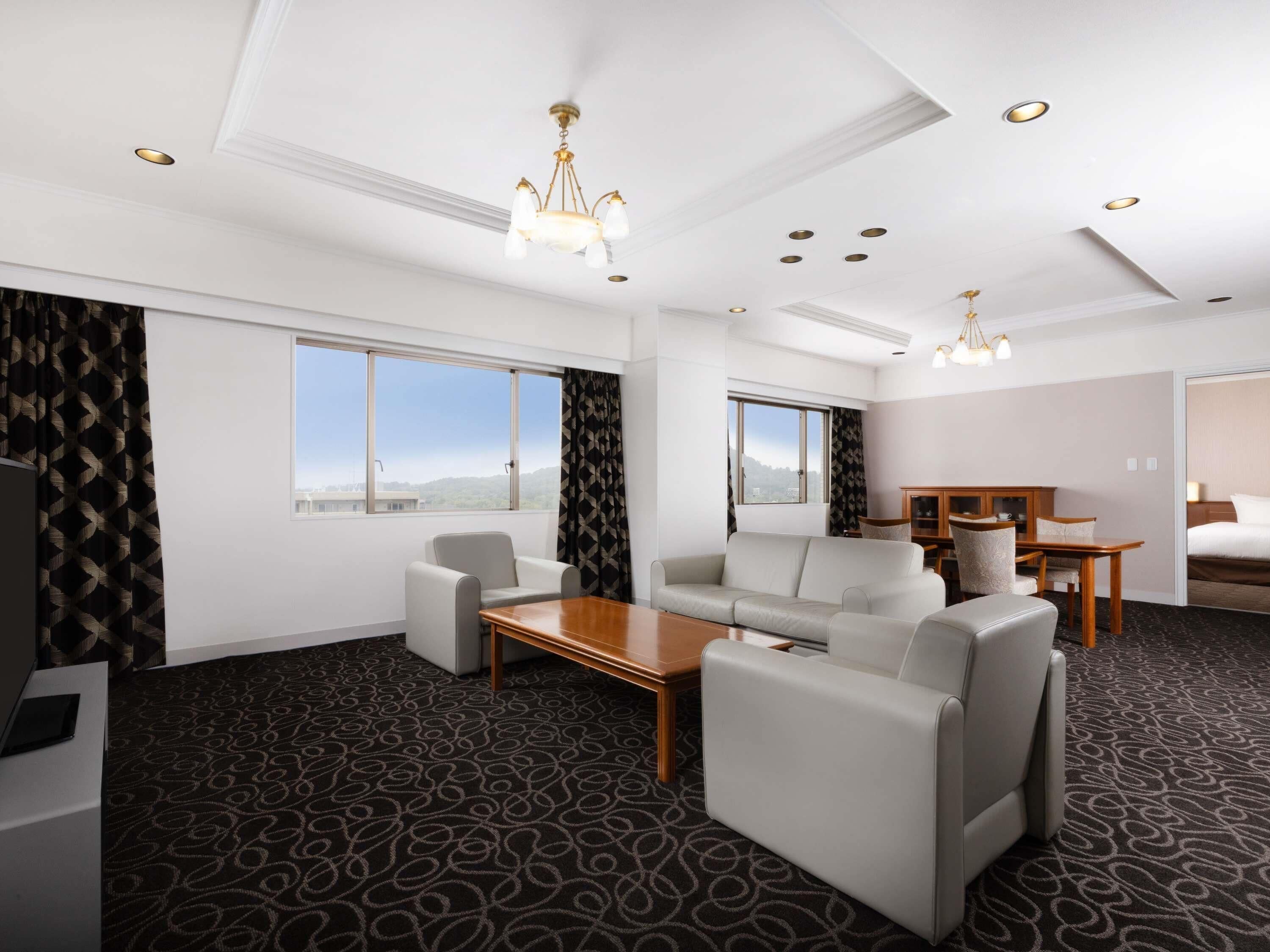 Una habitación de hotel con sofá, sillones, una mesa de centro de madera, escritorio y cama.