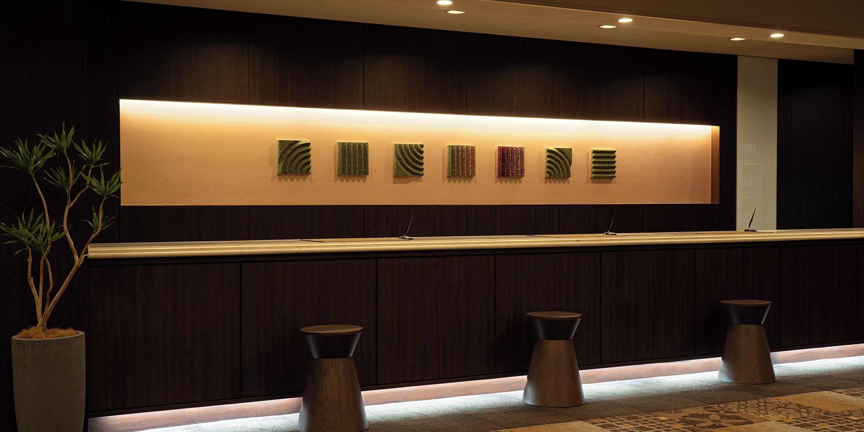A reception area with a long counter, a wall-mounted light, and three stools.