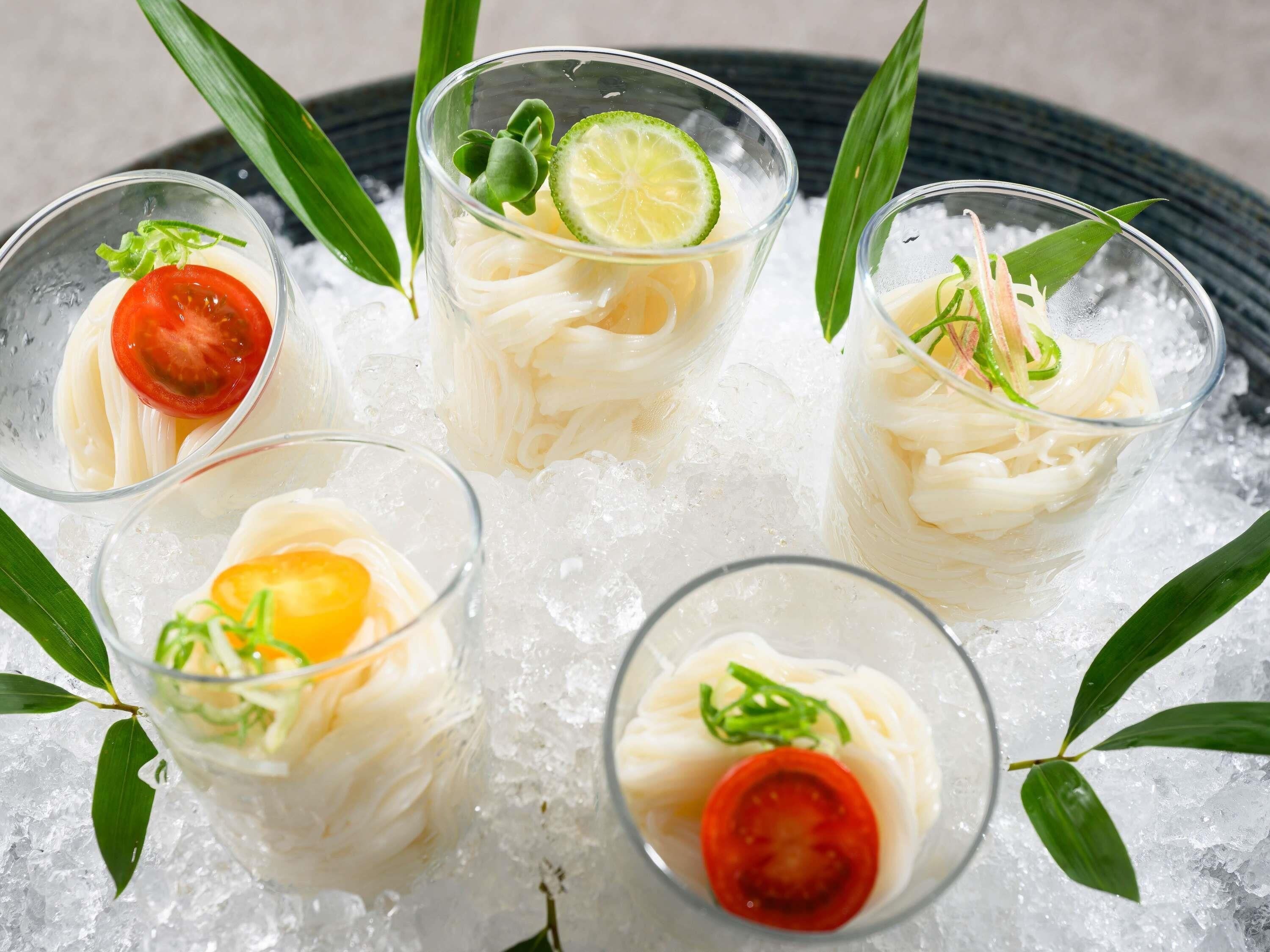 Five glasses of a white beverage with garnishes, served on ice.