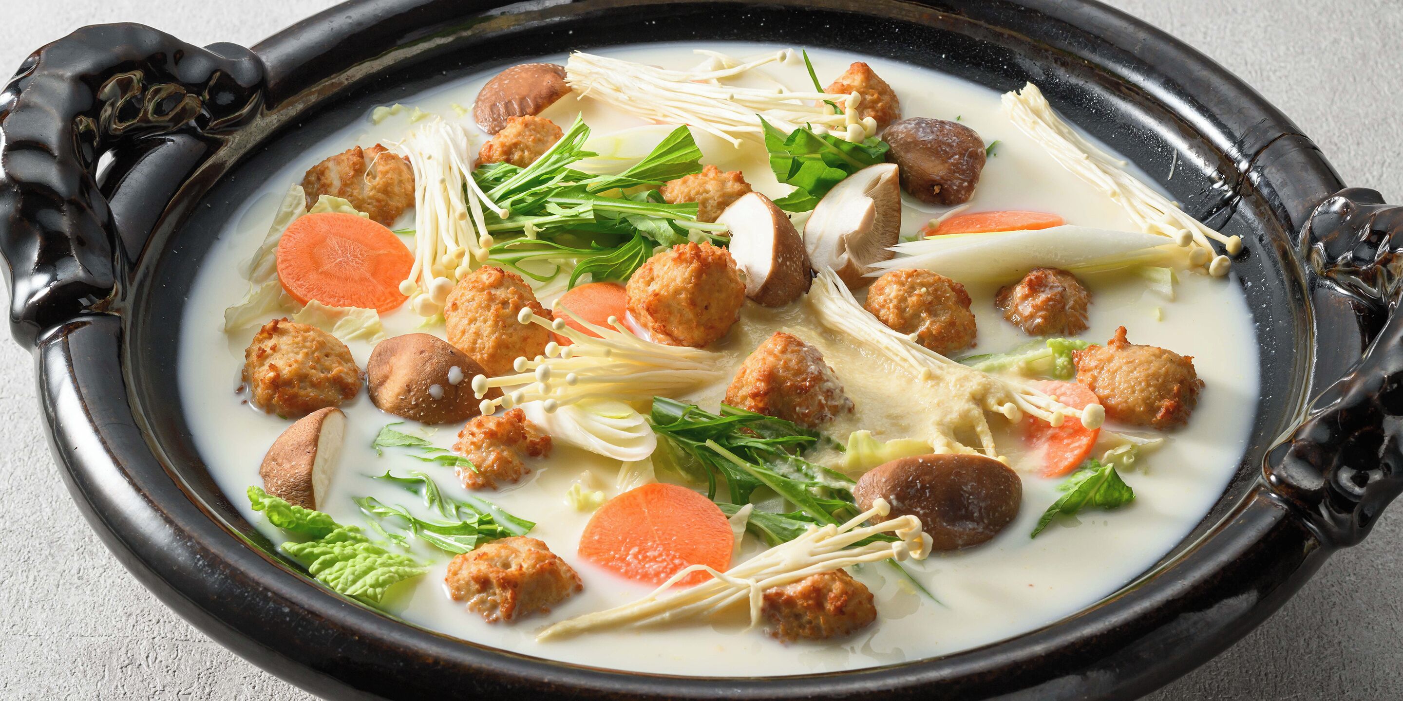 A traditional soup with various ingredients in a black ceramic bowl.