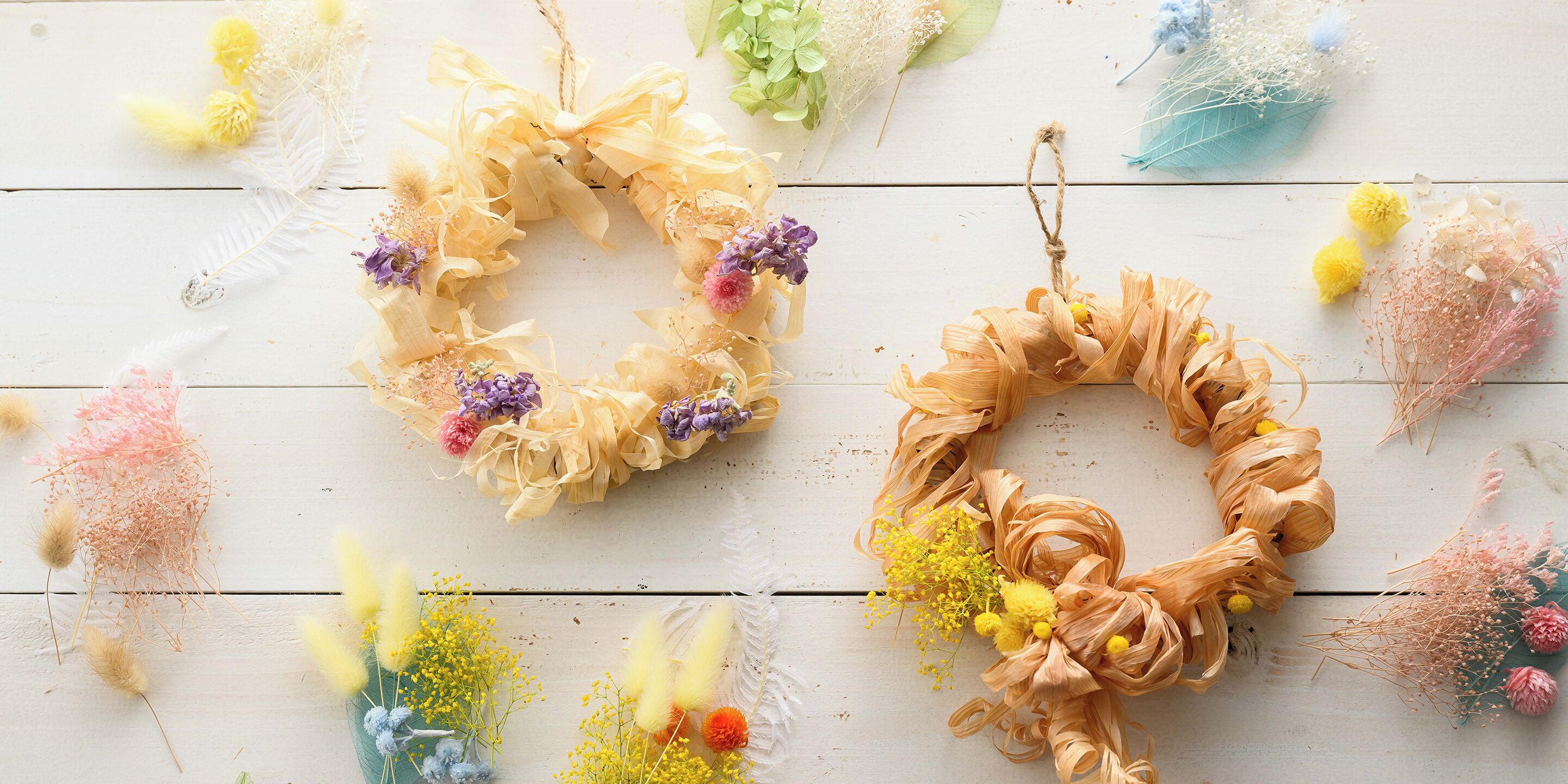 Zwei Kränze mit verschiedenen Blumen und Bändern auf einer Holzfläche.